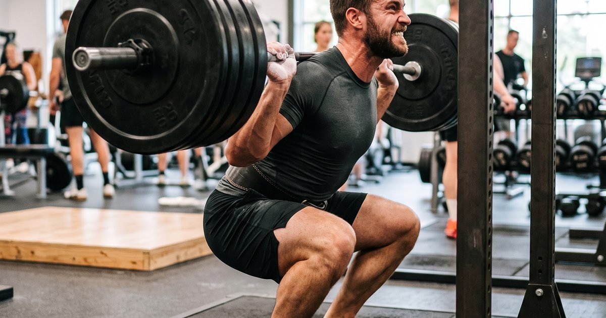 A lifter performing a heavy barbell back squat in a gym, feet planted, chalk on hands